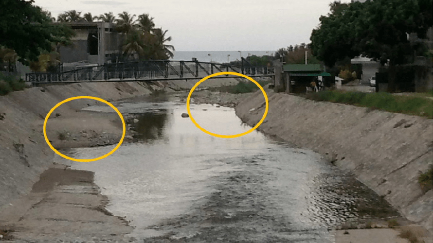Figura 26.Tramo inferior de la canalización en concreto del río Camurí Grande, vista hacia aguas abajo desde el puente en la Av. Costanera, mostrando acumulaciones de sedimentos en el lecho que explican las perturbaciones superficiales y los desbordes que ocurrieron hacia el Club Camurí Grande (foto del 12-09-2021).